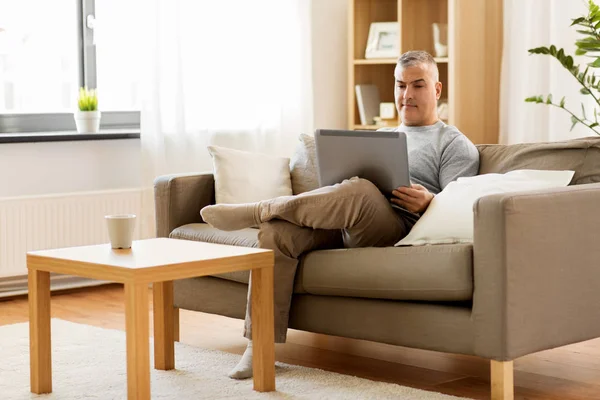 Uomo con computer portatile seduto sul divano di casa — Foto Stock