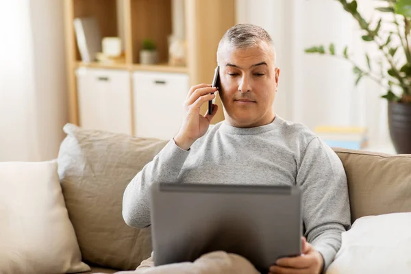 Mann mit Laptop telefoniert zu Hause mit Smartphone — Stockfoto