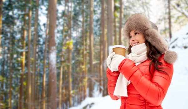 Жінка в хутряній шапці з кавою над зимовим лісом — стокове фото