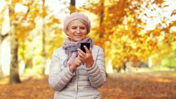 Mulher sênior feliz com smartphone no parque de outono — Vídeo de Stock
