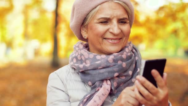 Šťastný senior žena s chytrým telefonem v podzimním parku — Stock video
