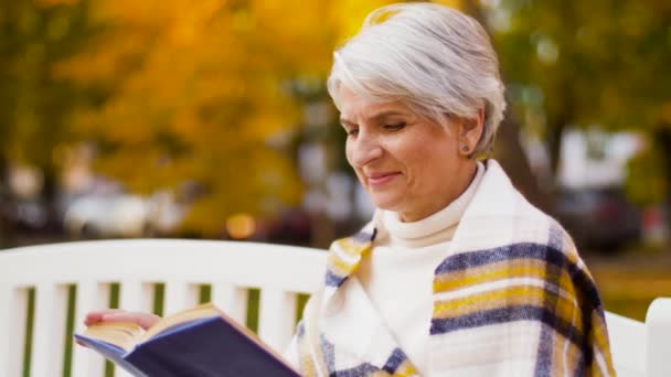 快乐的老妇人在秋天的公园看书 — 图库视频影像