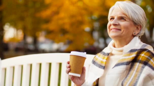Пожилая женщина пьет кофе в осеннем парке — стоковое видео