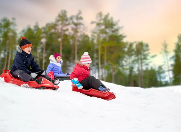 Crianças deslizando em trenós para baixo colina de neve no inverno — Fotografia de Stock
