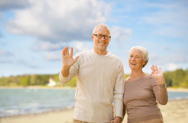 Happy senior couple waving hands on beach — Stock Photo, Image