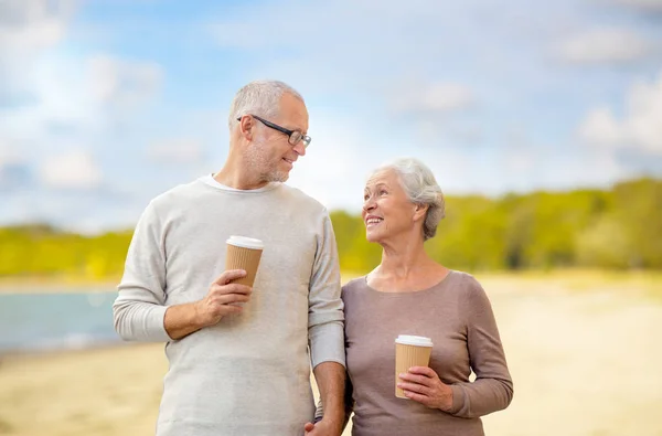 Senior couple with takeaway coffee on beach — Stock Photo, Image