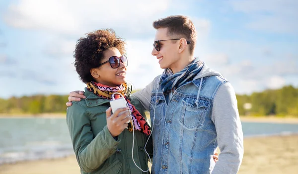 Casal com smartphone e fones de ouvido na praia — Fotografia de Stock