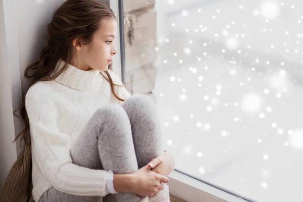 Verdrietig meisje zit op dorpel thuis venster in de winter — Stockfoto