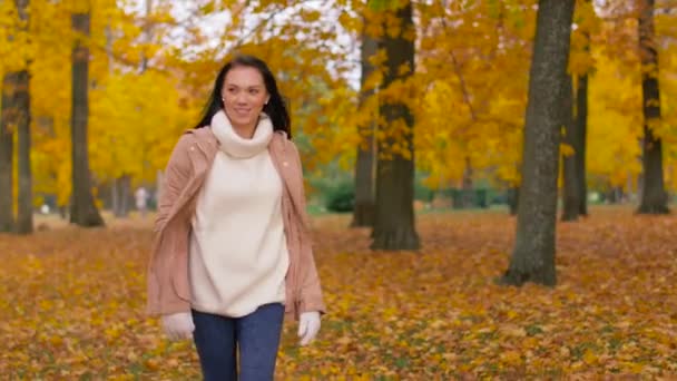 Щаслива молода жінка, що йде в осінньому парку — стокове відео