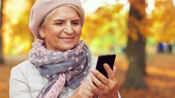 Mujer mayor feliz con teléfono inteligente en el parque de otoño — Vídeo de stock