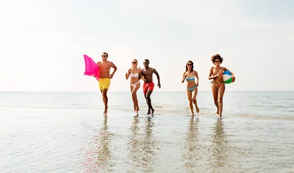 Freunde laufen mit Beachball und Badematratze — Stockfoto