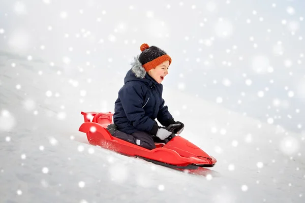 Menino feliz deslizando no trenó colina de neve no inverno — Fotografia de Stock