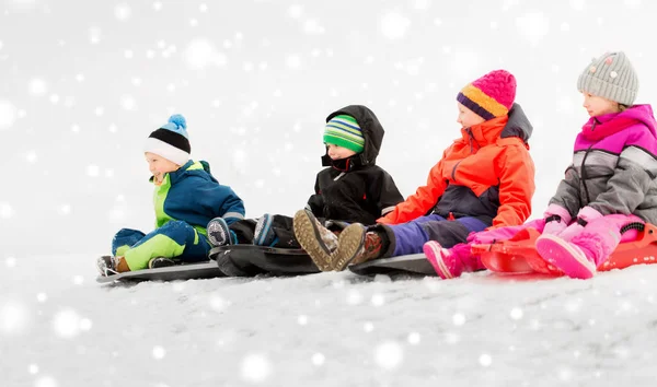 Glückliche kleine Kinder, die im Winter auf Schlitten rutschen — Stockfoto