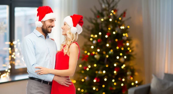 Feliz pareja en sombreros de Santa Claus abrazándose en Navidad —  Fotos de Stock