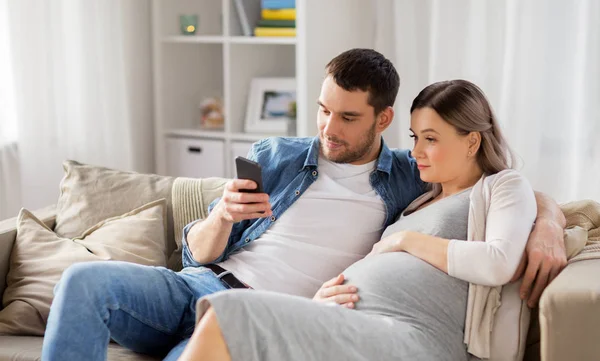 Hombre y esposa embarazada con teléfono inteligente en casa — Foto de Stock
