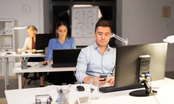 Hombre con teléfono inteligente que trabaja en la oficina nocturna —  Fotos de Stock