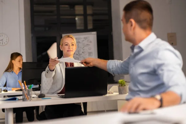 Mujer dando papeles a colega en la oficina nocturna — Foto de Stock