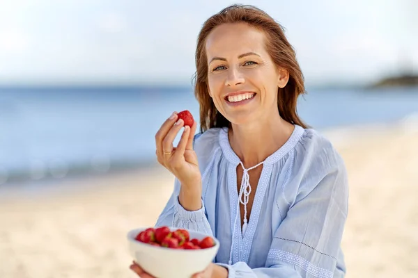 Ευτυχισμένη γυναίκα τρώει φράουλες σε παραλία το καλοκαίρι — Φωτογραφία Αρχείου