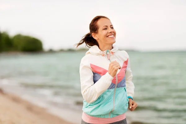 Lächelnde Frau läuft am Strand entlang — Stockfoto