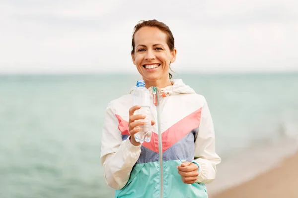 Mujer beber agua después de hacer ejercicio en la playa — Foto de Stock