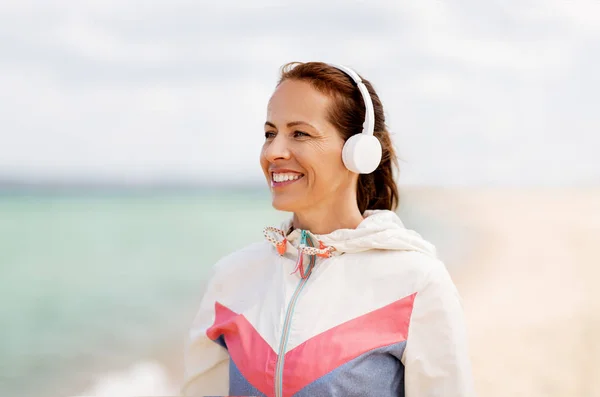 Femme souriante avec écouteurs sur la plage — Photo