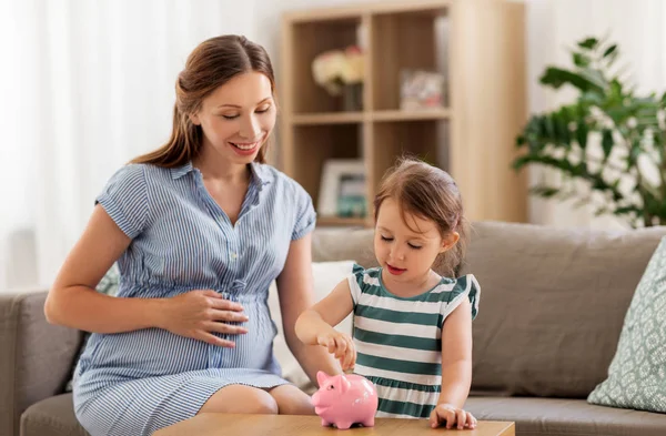 Pregnant mother and daughter with piggy bank — Stock Photo, Image