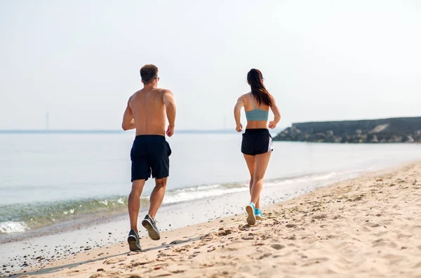 Pareja en ropa deportiva corriendo por la playa — Foto de Stock