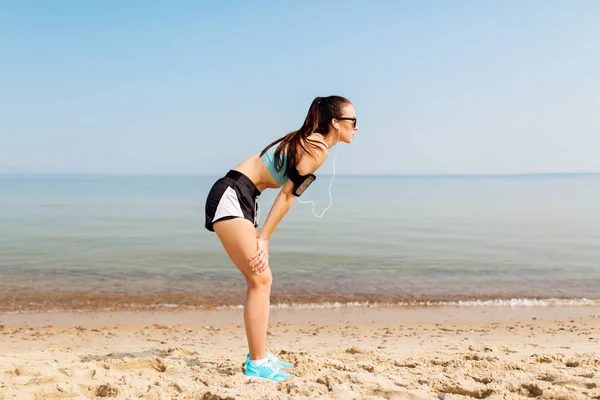 Vrouwelijke atleet met oortelefoons en armband op strand — Stockfoto