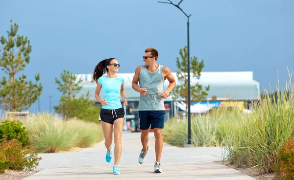 Pareja en ropa deportiva corriendo a lo largo de camino de playa — Foto de Stock