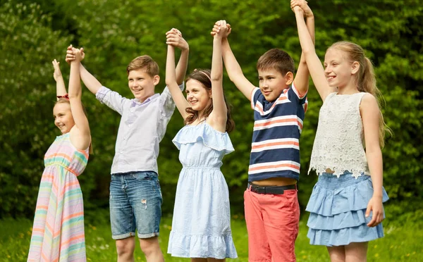 Crianças felizes segurando as mãos levantadas no parque de verão — Fotografia de Stock