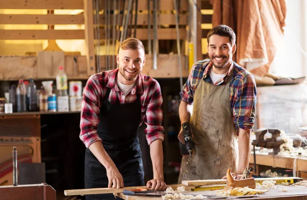 Carpinteros felices con taladro y tabla en el taller —  Fotos de Stock