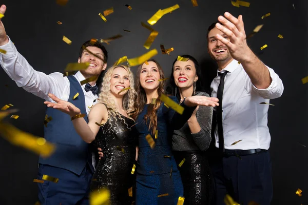 Amigos felizes na festa sob confete sobre preto — Fotografia de Stock