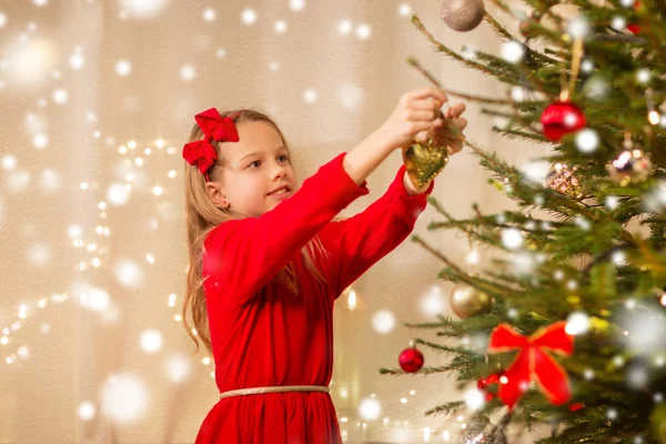 Gelukkig meisje in rood jurk versieren kerstboom — Stockfoto