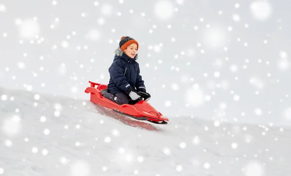 Niño feliz deslizándose en trineo colina abajo de la nieve en invierno — Foto de Stock