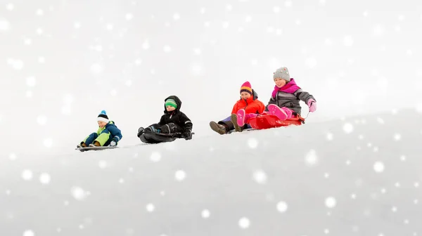 Bambini che scivolano sulle slitte giù per la collina di neve in inverno — Foto Stock