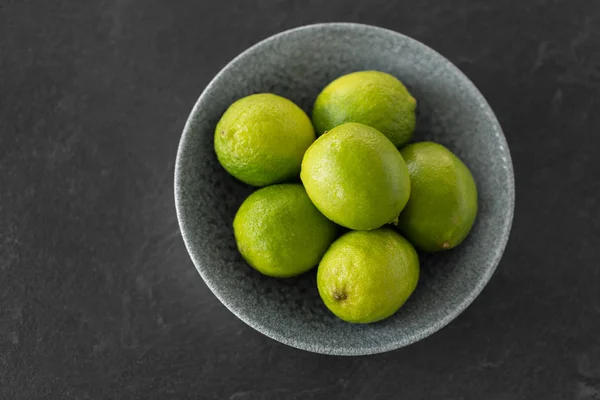 Close up of whole limes in bowl on slate table top — Stock Photo, Image