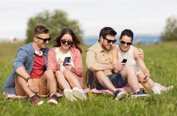 Ler vänner med smartphones sitter på gräset — Stockfoto