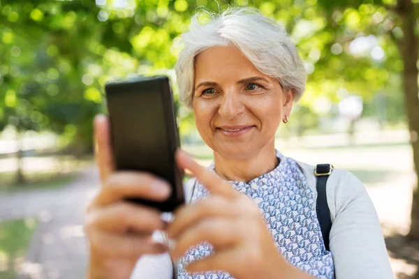 Senior kobieta fotografowanie przez komórki w lato park — Zdjęcie stockowe