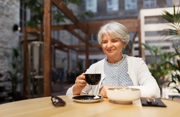 Старша жінка п'є каву на вуличному кафе — стокове фото