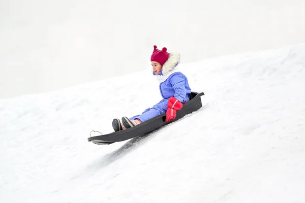 Gelukkig klein meisje glijden naar beneden op slee in de winter — Stockfoto