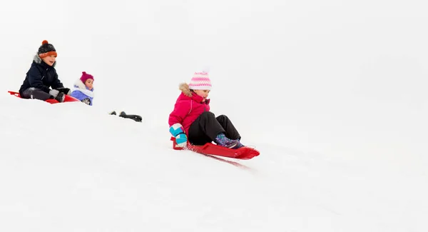 Kinder rutschen im Winter auf Schlitten den Schneehügel hinunter — Stockfoto