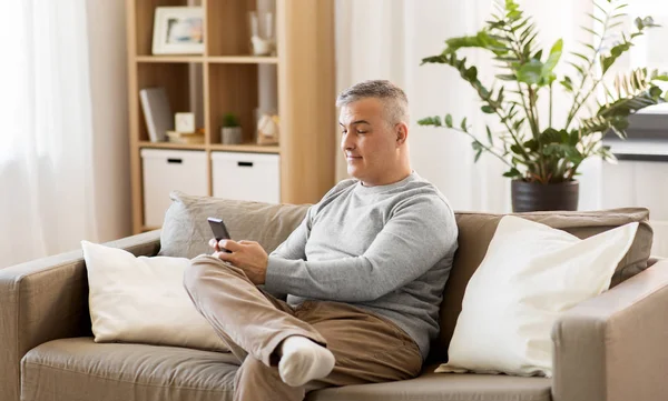 Homme avec smartphone assis sur le canapé à la maison — Photo