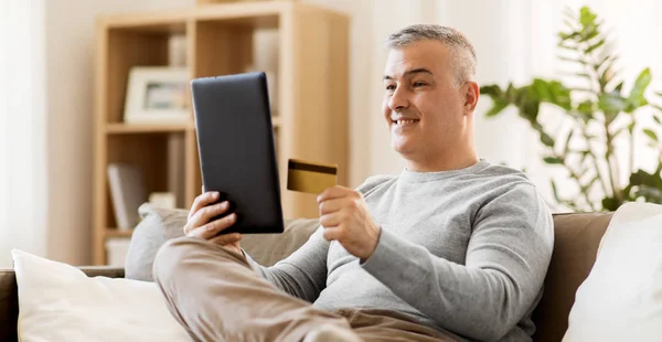 Hombre con tablet PC y tarjeta de crédito en el sofá en casa —  Fotos de Stock