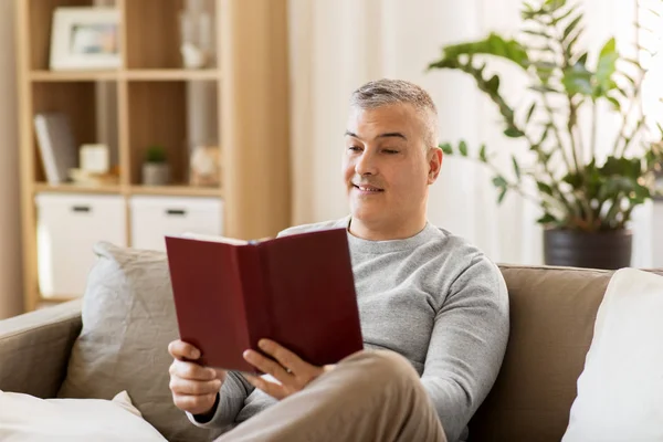 Kanepede oturan ve evde kitap okurken erkek — Stok fotoğraf