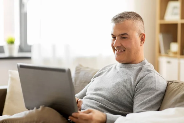 Uomo con computer portatile seduto sul divano di casa — Foto Stock