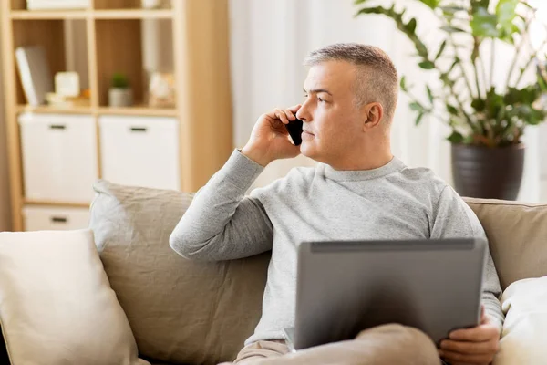 Mannen med laptop uppmanar smartphone hemma — Stockfoto