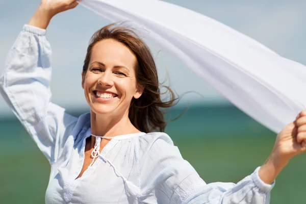 Mulher feliz com xale acenando no vento na praia — Fotografia de Stock