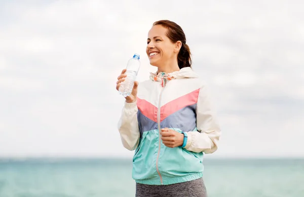 Женщина пьет воду после тренировки на берегу моря — стоковое фото