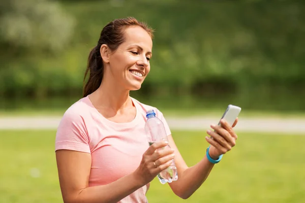 Mulher com água potável smartphone no parque — Fotografia de Stock