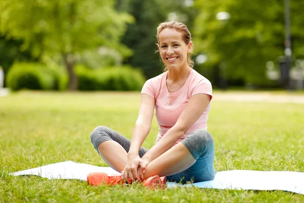 Kvinna sitter på träningsmatta på park i sommar — Stockfoto